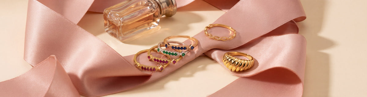Dainty gold rings nestled in blush silk ribbon beside a perfume bottle