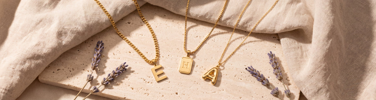 Gold initial necklaces with letter pendants on travertine with dried lavender