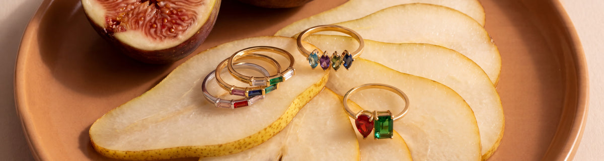 Gold birthstone rings resting on pear slices and fig