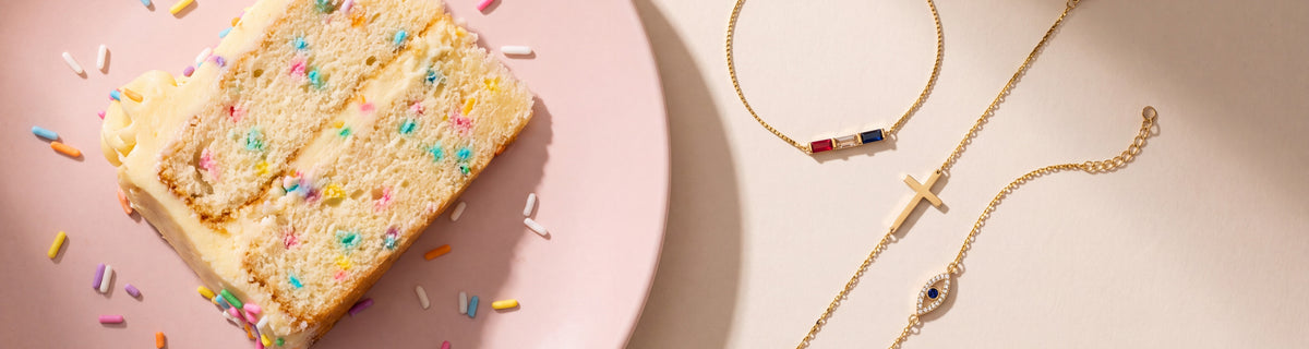 Dainty birthstone, cross and evil eye bracelets beside a slice of birthday cake