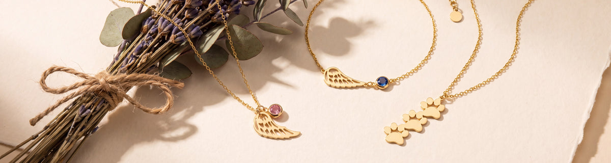 Angel wing and paw print memorial jewelry beside dried lavender and eucalyptus