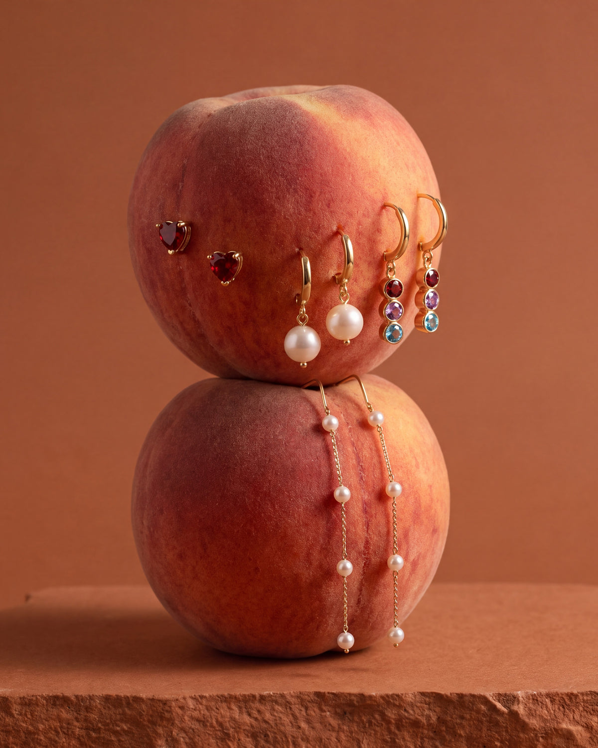 Gold heart, pearl and birthstone earrings on peaches