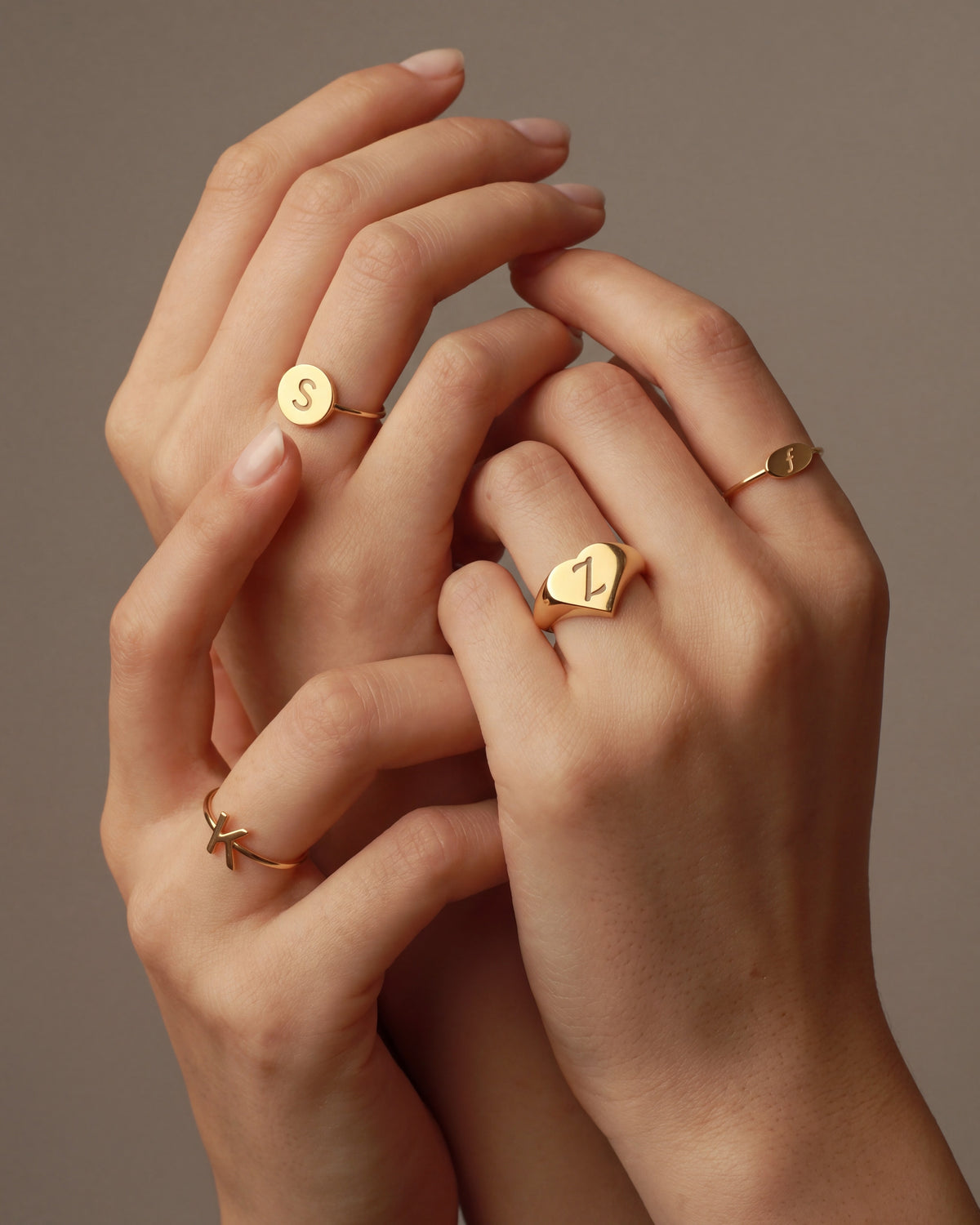 Gold initial signet rings on interlaced hands
