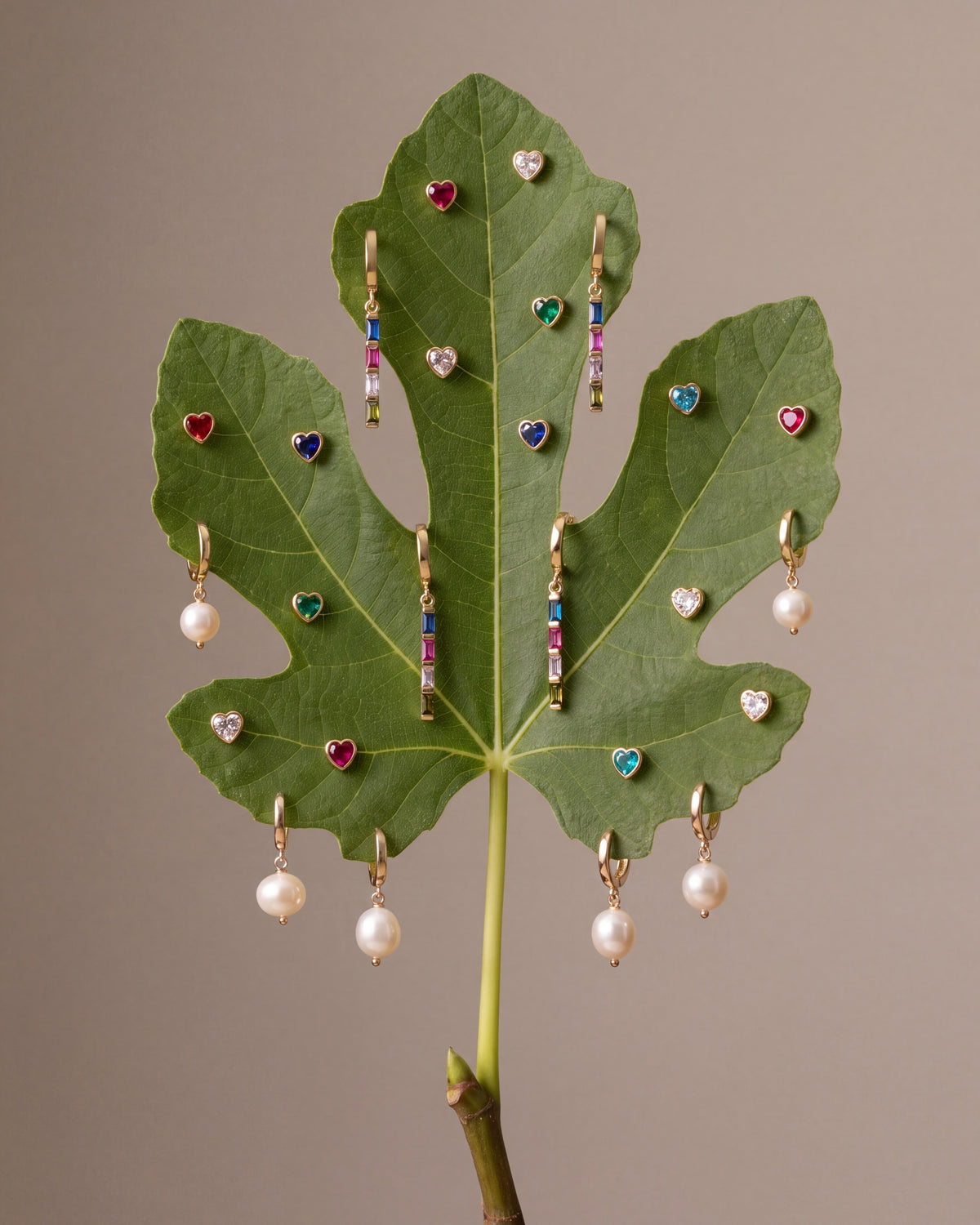 Pearl and birthstone earrings arranged on a fig leaf